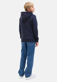 Marineblaues Hoodie mit Kordelzugkapuze, lockere Passform; kombiniert mit weit geschnittenen blauen Jeans und weißen Sneakers. Glatter Stoff, lässiges Design.