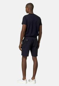 T-shirt a maniche corte color navy abbinato a pantaloni corti neri, realizzato in tessuto traspirante. Il modello indossa sneakers bianche senza loghi o fantasie visibili.