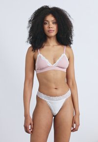 Jasnoróżowy stanik z koronkowym wykończeniem i biały thong z koronkowymi akcentami. Miękka, gładka tkanina z falbaniastymi brzegami. Prosty design i kontrast kolorystyczny.