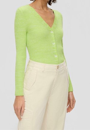 Frau trägt eine gerippte limettengrüne V-Ausschnitt-Strickjacke mit Knöpfen, kombiniert mit hoch taillierten cremefarbenen Cargo-Hosen.