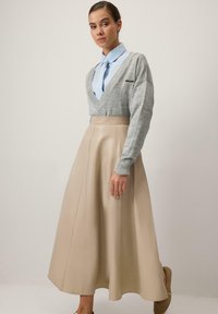 Halli V-kaelusega kampsun soonikkoes varrukateäärega, kombineeritud kõrge vöökohaga beežast nahast seelikuga. Sile tekstuur, voolav disain ja põlvekõrgune pikkus.