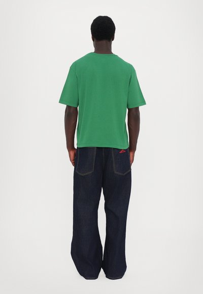 Grønn bomull t-skjorte med avslappet passform og korte ermer, kombinert med mørkeblå vide jeans med synlig søm og baklommer.