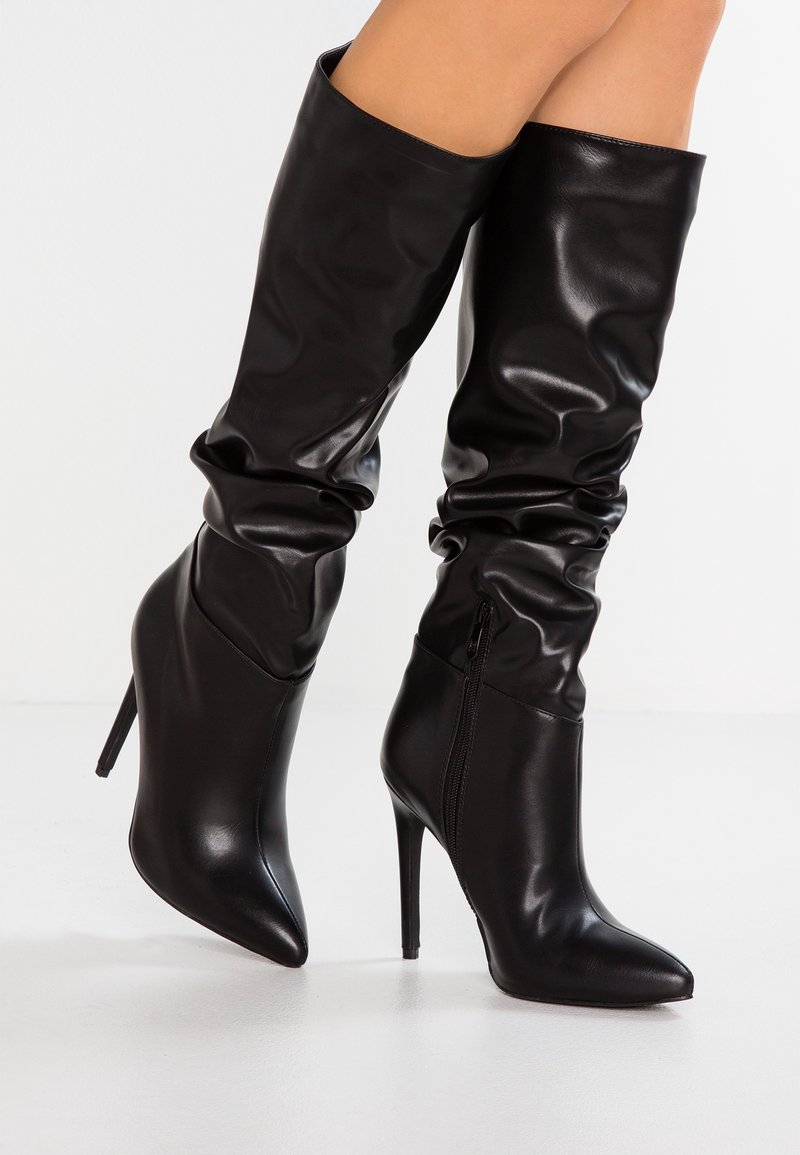 Botas de cuero negro hasta la rodilla con un diseño despeinado, punta afilada y tacón alto tipo stiletto; cuentan con una cremallera lateral para ponerlas y quitarlas fácilmente.