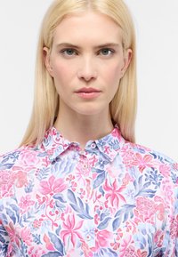 Camicia a bottoni floreale con base bianca, caratterizzata da stampe botaniche rosa e blu, colletto classico e bottoni visibili.