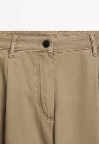 Beżowe bawełniane spodnie z zapięciem na guzik, kieszeniami z przodu i gładką fakturą. Charakteryzują się klasycznym designem z precyzyjnymi detalami szycia.