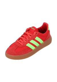 Scarpe da ginnastica rosse con dettagli verdi e tre righe. Realizzate in suede e mesh, presentano una suola in gomma e un design con lacci.