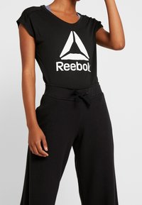 Černé tričko Reebok s bílým logem, krátké rukávy a volný střih, spárované s černými tepláky s pasem na šňůrku.