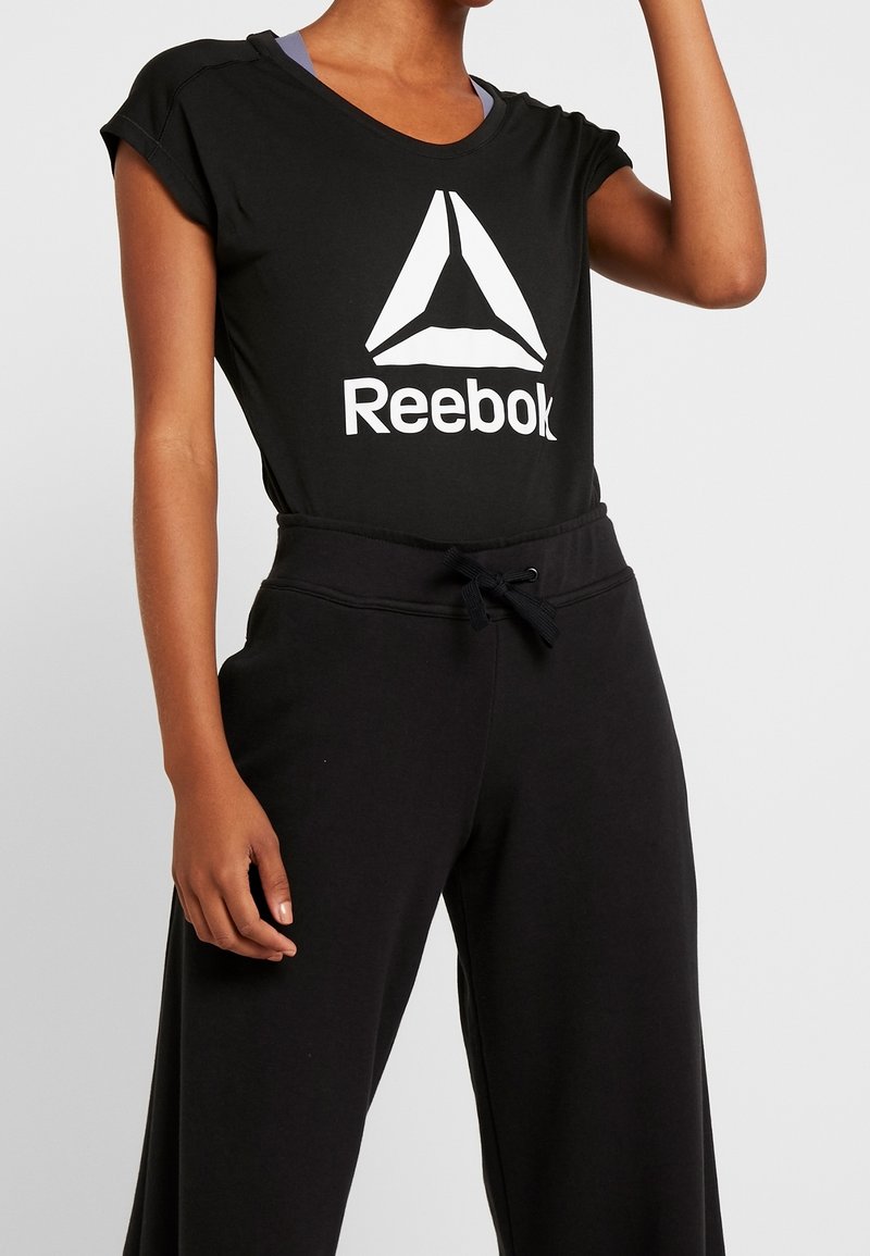 Černé tričko Reebok s bílým logem, krátké rukávy a volný střih, spárované s černými tepláky s pasem na šňůrku.