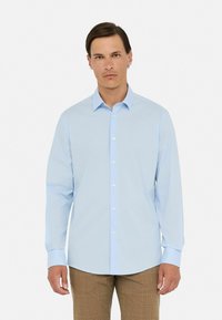 Camisa de manga larga azul claro con botones en el frente, cuello clásico y textura suave, combinada con pantalones de cuadros marrones.