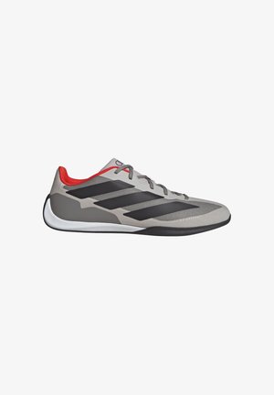 Zapatilla deportiva gris con diseño de rayas negras, acentos rojos en el talón, parte superior texturizada y suela blanca. Cordones planos incluidos.