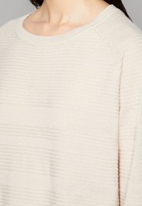 Maglione color beige chiaro con un motivo a righe testurizzato, colletto rotondo e maniche raglan, realizzato in un morbido tessuto lavorato a maglia.