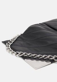 Czarna pikowana skórzana torebka na ramię z dużym srebrnym łańcuchem i srebrnym trójkątnym zapięciem wygrawerowanym napisem "DKNY."
