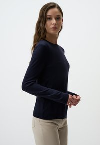 Maglione lavorato a maglia blu navy con maniche lunghe, collo rotondo, polsini e orlo a coste. Indossato sopra pantaloni beige, caratterizzati da una texture liscia.