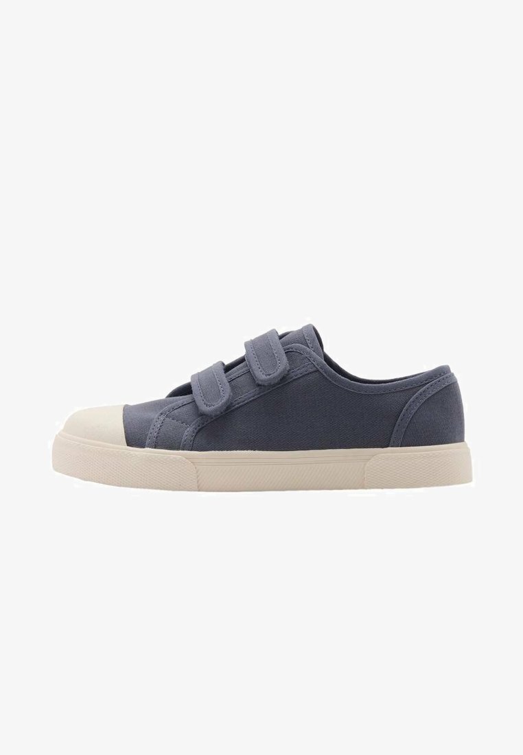 Gray canvas sneaker with two Velcro straps, a cream rubber toe cap, and a textured sole. Low-profile design with rounded shape.