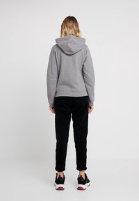 Sudadera gris con un bolsillo canguro, puños y dobladillo acanalados. Combinada con pantalones de pana negros y zapatillas negras con suelas blancas.