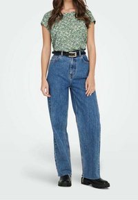 Top verde floreale a maniche corte, jeans blu a vita alta, cintura nera e stivaletti neri chunky alla caviglia. Look casual con denim morbido.