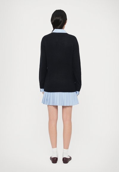 Sötétkék kötött pulóver lekerekített nyakkivágással, világoskék plisszírozott ruhával párosítva. Hosszú ujjú, bordázott mandzsettával, sima textúrájú.