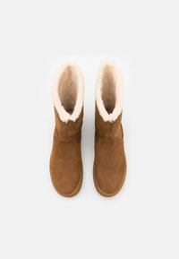 Bottes d'hiver en daim marron avec doublure en polaire blanche, vues de dessus sur fond blanc.