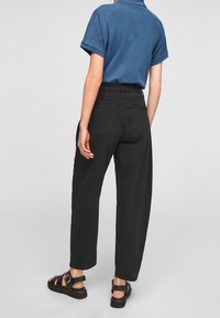 Černé kalhoty s vysokým pasem a volným střihem, pět kapes a hladká textura, doplněné modrou košilí s krátkým rukávem a černými sandály.