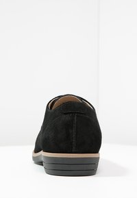 Scarpa in suede nera con punta rotonda, tacco basso e finitura testurizzata. La suola presenta un design a strati con un accento color terra.