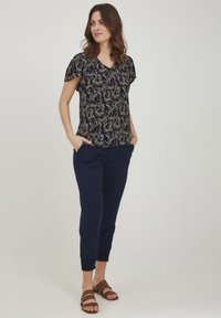 Top blu navy con motivo floreale dorato, maniche corte e scollatura a V. Abbinato a pantaloni jogger blu navy e sandali con cinturini marroni.