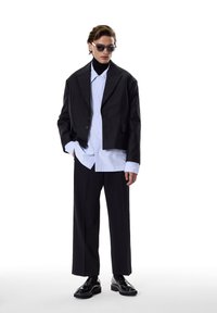 Black cropped blazer over a light blue oversized shirt, paired with black wide trousers and shiny black shoes. Accessories include sunglasses.