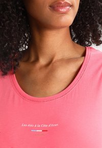 Rosa Baumwoll-T-Shirt mit einem runden Halsausschnitt und dezenten Nähten. Textdesign in Weiß und bunten Streifen unterhalb des Halsausschnitts.