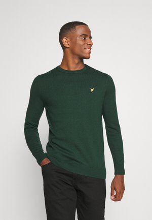 Maglione lavorato a maglia verde scuro con scollatura rotonda, polsini e orlo a coste; presenta un piccolo logo dorato sul petto; texture liscia.