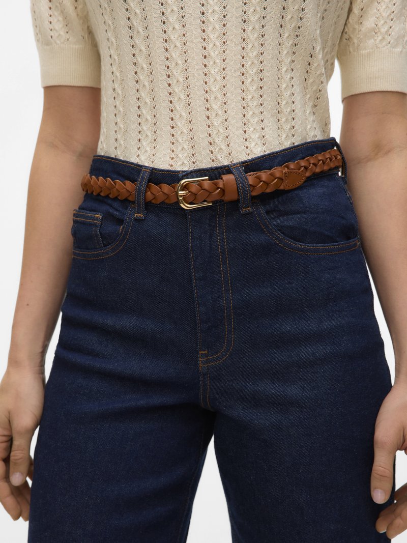 Μπεζ πλεκτό τοπ με κοντά μανίκια, μπουζωμένο σε ψηλόμεσο σκούρο μπλε τζιν με καφέ πλεκτή δερμάτινη ζώνη και χρυσή αγκράφα.