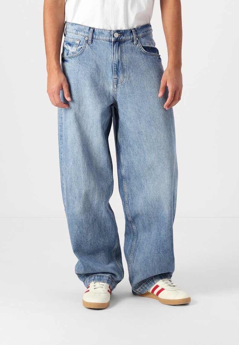 Jean en denim bleu clair avec une coupe décontractée et ample, légèrement délavé. Dispose de cinq poches, de coutures robustes et d'une fermeture à bouton en métal.