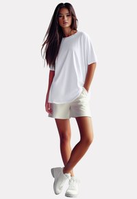 T-shirt bianca oversize con scollatura rotonda, abbinata a pantaloni corti beige e sneakers bianche. Tessuto morbido e vestibilità rilassata.