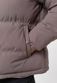 Kurtka puchowa w jasnym mauve o gładkiej teksturze, z boczną kieszenią z zatrzaskiem oraz elastycznymi mankietami zapewniającymi dobre dopasowanie.