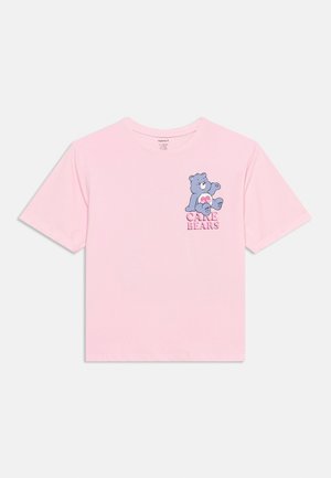 T-shirt rose clair à manches courtes avec un personnage bleu des Care Bears assis tenant un cœur rose, avec le texte "Care Bears" en dessous sur la poitrine.