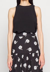 Top negro sin mangas combinado con una falda negra con patrones florales blancos; tejido suave, cintura ajustada y parte inferior acampanada.