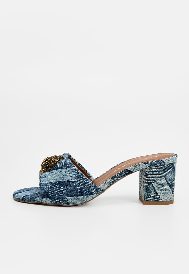 Mule de tacón bloque de denim con textura tejida, punta abierta y adornos decorativos en la parte superior. Color predominantemente azul con tonalidades variadas.