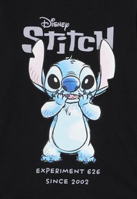 Černé tričko s krátkým rukávem, na kterém je kreslený obrázek Stitcha, modrého mimozemšťana s velkýma očima a ušima, a text "Disney Stitch" a "Experiment 626 Od 2002."
