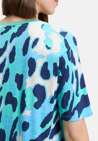 Short-sleeve top in a blue and green animal print, featuring a round neckline and soft, textured fabric with a slight sheen.