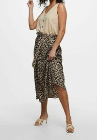 Top beige senza maniche con bottoni, abbinato a una gonna midi con stampa leopardata e orlo asimmetrico. Indossato con sandali con tacco di colore chiaro.