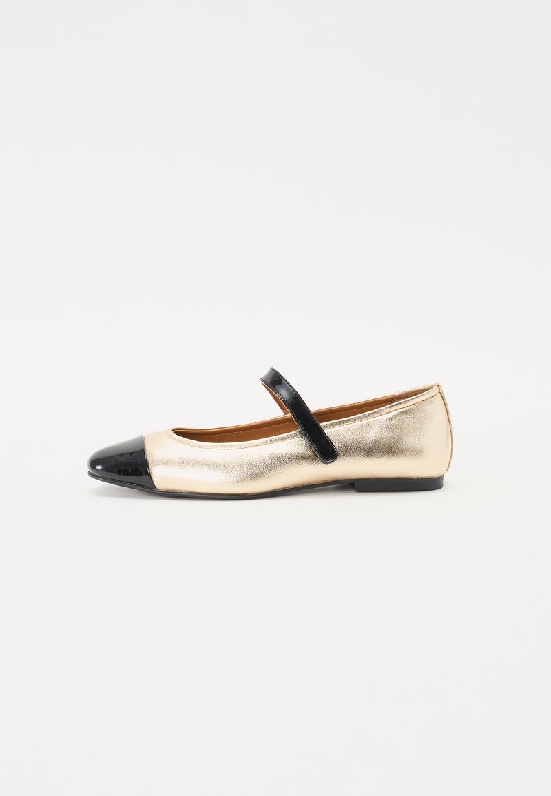 Bailarina metálica dorada con puntera de charol negro y correa ajustable. Textura suave, tacón bajo y forma redondeada.