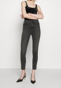 Högmidjade svarta jeans med skinny fit, fransade fållar och subtil blekning, kombinerade med en svart sammetslinne och svarta klackar.