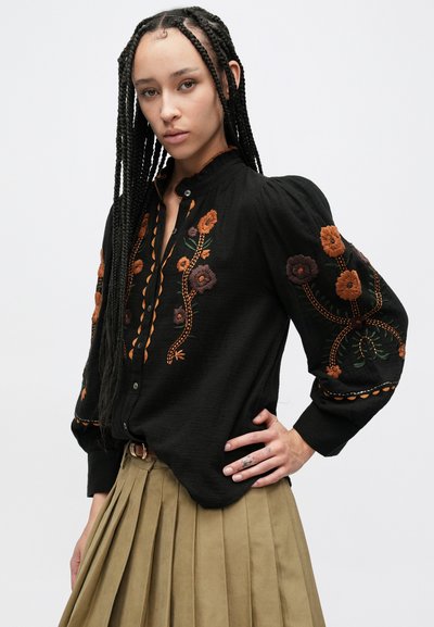 Črna bluza s srajčnimi gumbi in nabranimi rokavi, z večbarvnimi cvetličnimi vezeninami in okrasnimi šivi spredaj in na manšetah.