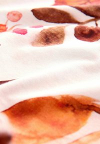 Stof met een witte achtergrond en abstracte patronen in oranje, bruin en roze. Het materiaal lijkt glad en zacht met een subtiele textuur.