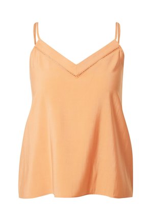 Kobieta w brzoskwiniowych spodniach o szerokich nogawkach i dopasowanym topie na cienkich ramiączkach, w towarzystwie białych sandałów na wysokim obcasie z paskami.