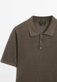 Poloko s krátkým rukávem v tmavě hnědé pletenině s klasickým límcem, třemi knoflíky a jemnou texturou. Značkový štítek viditelný uvnitř límce.