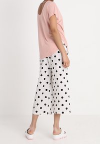 Lyserød kortærmet bluse med udsnit bagpå, parret med vide hvide bukser med store sorte prikker. Hvide sko.