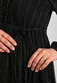 Svart klänning med silver vertikala ränder, knytliv, lång ärm och matchad med ringar med guldaccent och en ljus manikyr.