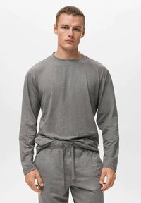 Top de manga larga gris con escote redondo, hecho de una tela suave, emparejado con pantalones con cordón a juego. Diseño simple y casual.