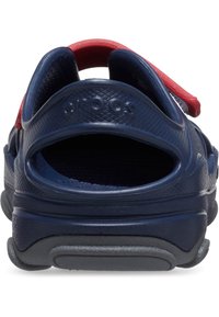 Crocs blu navy con un design testurizzato, apertura posteriore e cinturino rosso sul tallone. Presentano una suola imbottita e un marchio in rilievo sul lato.