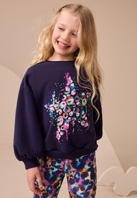 Navy sweatshirt with sequined, multicolored abstract design, paired with patterned leggings in vibrant hues of blue, purple, and pink.