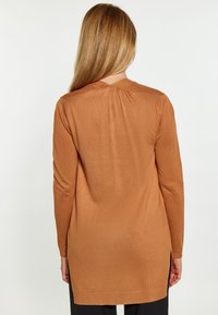 Bluză din tricot cu mânecă lungă, de culoare maro, având un plisat în spate și fante laterale la margine pentru un detaliu suplimentar. Textură fină, material ușor.